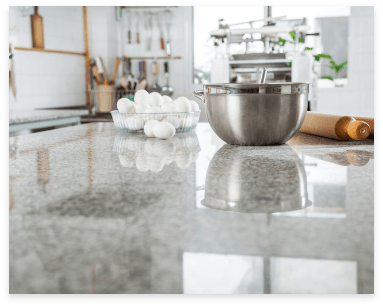 A kitchen counter with a bowl of eggs and a mixing bowl on natural marble countertops.