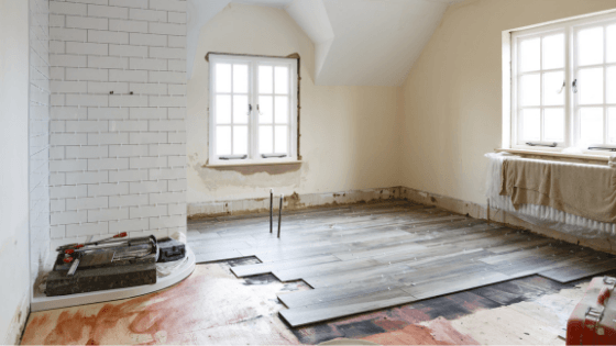 Bright, partially renovated room with white walls and unfinished wood flooring. Two large windows provide natural light. Tools are scattered on the floor.