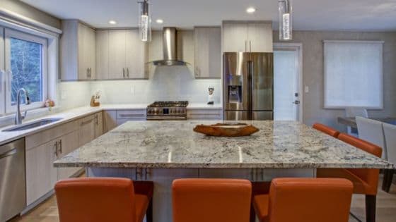 Modern kitchen with marble island countertop, four orange chairs, stainless steel appliances, and soft lighting. Cozy and stylish ambiance.