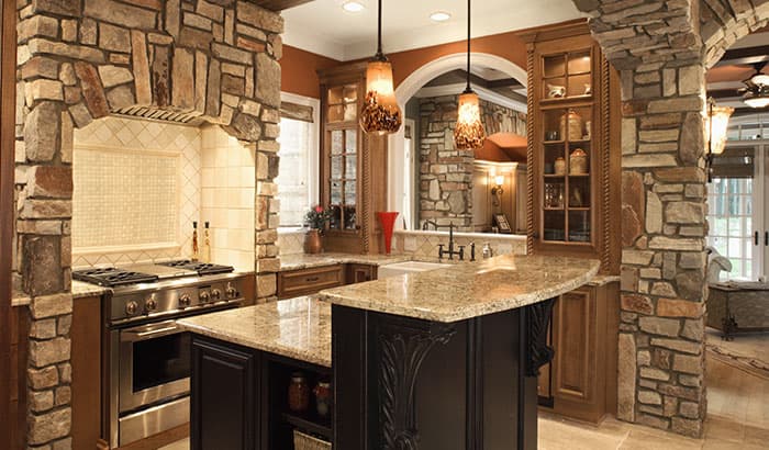Rustic kitchen with stone walls, wooden cabinets, granite countertops, and warm pendant lighting. Cozy and inviting ambiance.