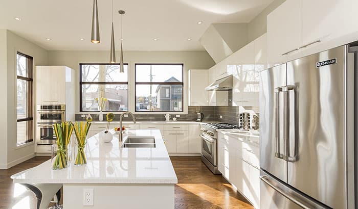 Modern kitchen with white cabinets, stainless steel appliances, and a large island. Sunlight streams through large windows, creating a bright, airy atmosphere.