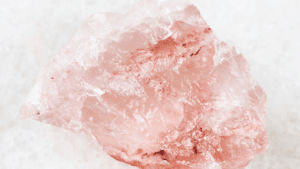 A large raw rose quartz crystal with a soft pink hue and rough texture, set against a light background. It conveys a sense of natural beauty and tranquility.