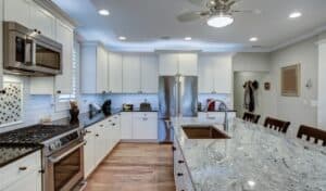 Modern kitchen with a large granite island, bar stools, stainless steel appliances, and white cabinetry. The space is bright and inviting.