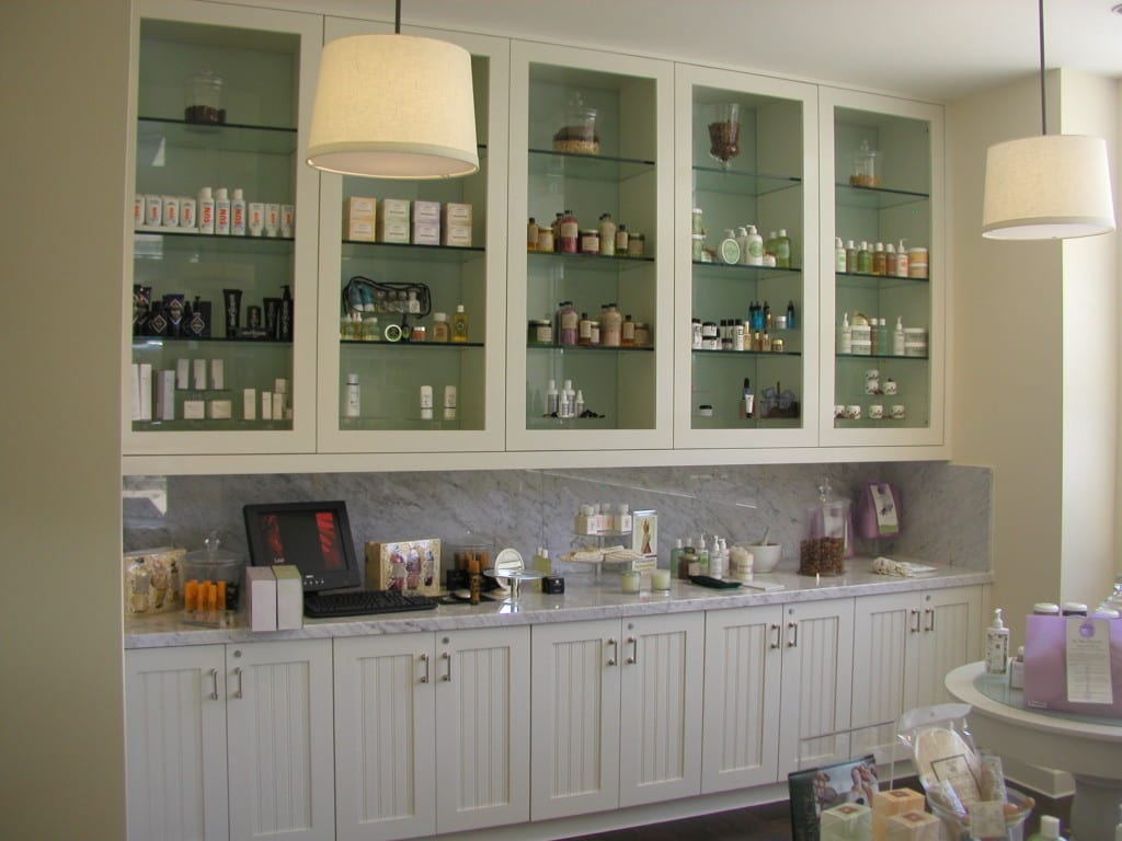 A white cabinet displaying numerous bottles, highlighting custom countertops designed for a beauty supply shop.