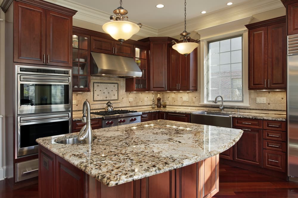 Spacious kitchen with rich cherry wood cabinets, granite countertops, and stainless steel appliances. Large island with sink, under warm pendant lighting.