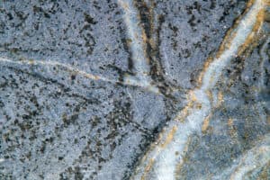 Close-up of a textured stone surface with intersecting lines and speckles. Gray and beige tones create an intricate, natural abstract pattern.
