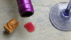 A wine glass and cork on a table, with tips on removing stains from stone countertops.