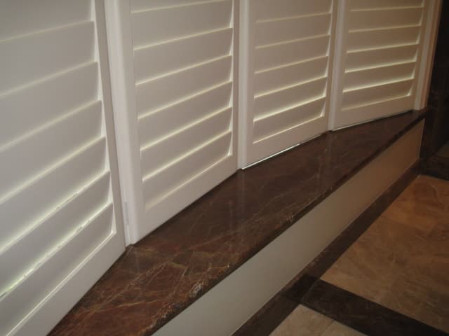 A window adorned with white shutters, complemented by a sleek marble counter beneath it, creating an elegant interior view.