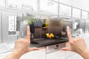 Hands frame a modern kitchen transitioning from sketch to reality, highlighting a sleek counter with a sink, fruit bowl, and stove. Tone: creative and transformative.