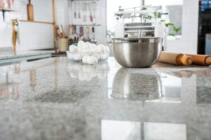 A modern kitchen with a reflective granite countertop, featuring a metal bowl, a rolling pin, and a glass bowl filled with eggs. The ambiance is clean and organized.