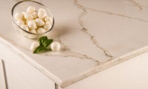 A bowl filled with white cheese and fresh basil is placed on a polished quartz countertop.