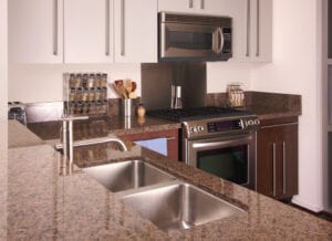 Modern kitchen with granite countertops, stainless steel sink and appliances, including an oven and microwave. Neatly arranged spice rack, utensils, and a pepper mill add a tidy, functional feel.