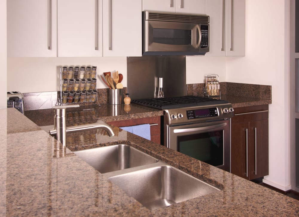 Modern kitchen with granite countertops, stainless steel sink and appliances, including an oven and microwave. Neatly arranged spice rack, utensils, and a pepper mill add a tidy, functional feel.