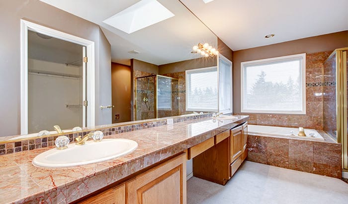 Bright bathroom with marble countertop, dual sinks, wooden cabinets, and a large mirror. Features a glass shower, bathtub, and skylight. Luxurious feel.