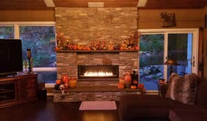 A cozy living room featuring a stone fireplace and a comfortable couch, with a glimpse of the adjoining kitchen.