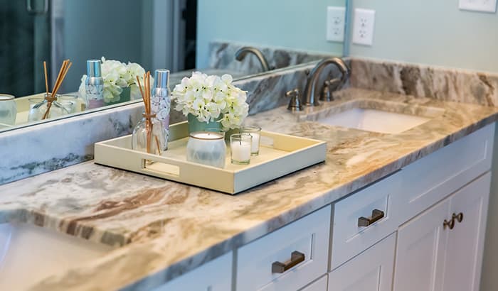 Marble bathroom vanity with dual sinks, a tray holding a candle, diffuser, and white flowers, all creating a serene and elegant ambiance.