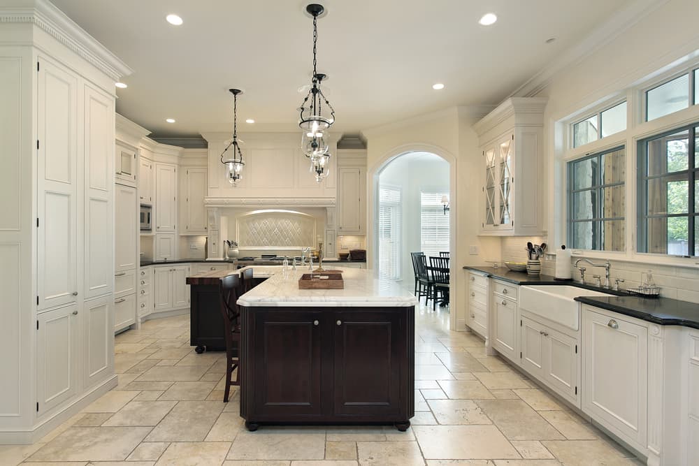 Elegant kitchen with white cabinetry, dark wood island, and marble countertops. Three pendant lights hang above. Large window and archway enhance space.
