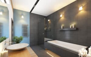 Modern bathroom with dark gray tiles, white bathtub, and a wooden vanity with a round sink. Soft lighting and candles create a calm ambiance.
