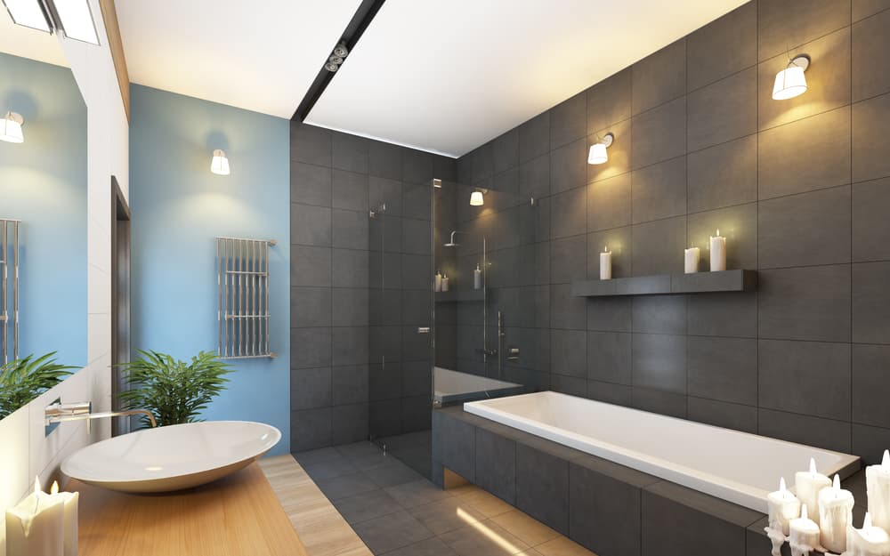 Modern bathroom with dark gray tiles, white bathtub, and a wooden vanity with a round sink. Soft lighting and candles create a calm ambiance.