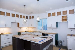 Modern kitchen under renovation with white cabinets, two pendant lights above a large island, and walls partly painted. Calm, organized ambiance.