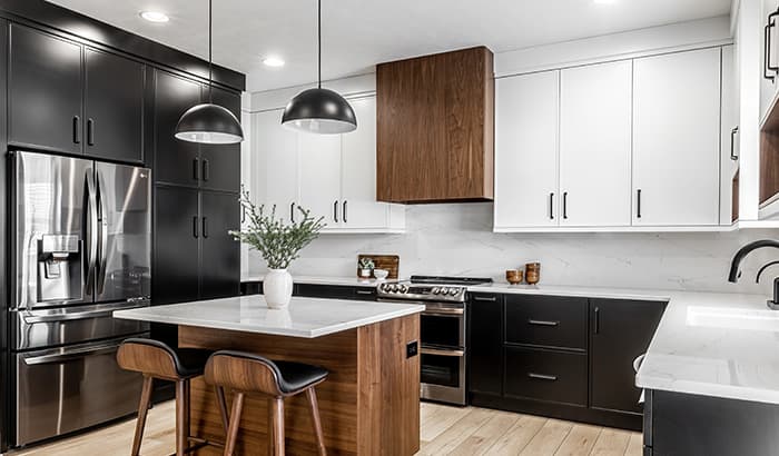 Modern kitchen with sleek black and white cabinetry, stainless steel appliances, and wood accents. An island with pendant lights and stools adds warmth.