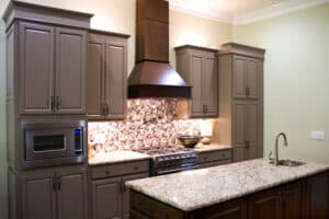 Modern kitchen with taupe cabinets, granite countertops, and stainless steel appliances. Mosaic tile backsplash and sleek vent hood above the stove.