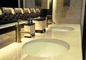 Luxurious bathroom with two round sinks in a marble counter, bronze faucets, ornate mirror, and elegant soap dispensers; warm, sophisticated ambiance.