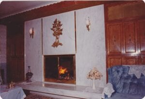 A warm fireplace with a mantle and a blue chair in front.