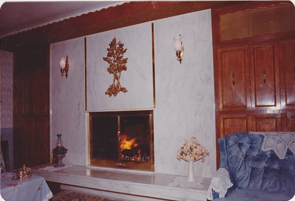 A warm fireplace with a mantle and a blue chair in front.