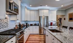 Modern kitchen with white cabinets, stainless steel appliances, and a granite island countertop. Brightly lit with wooden floors and a cozy ambiance.
