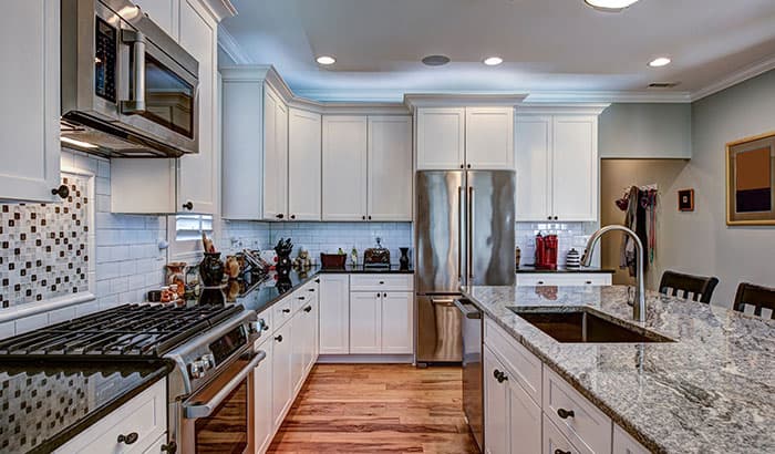 Modern kitchen with white cabinets, stainless steel appliances, and a granite island countertop. Brightly lit with wooden floors and a cozy ambiance.