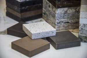 A selection of stone countertop samples in various colors and textures, including speckled white and different shades of brown, stacked on a surface.