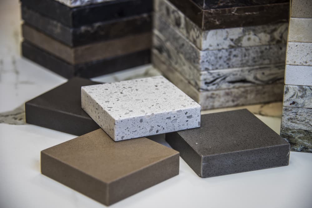 A selection of stone countertop samples in various colors and textures, including speckled white and different shades of brown, stacked on a surface.
