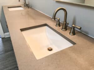 Modern bathroom with dual sinks, sleek beige countertop, and brushed nickel fixtures against a neutral wall, creating a clean, elegant atmosphere.