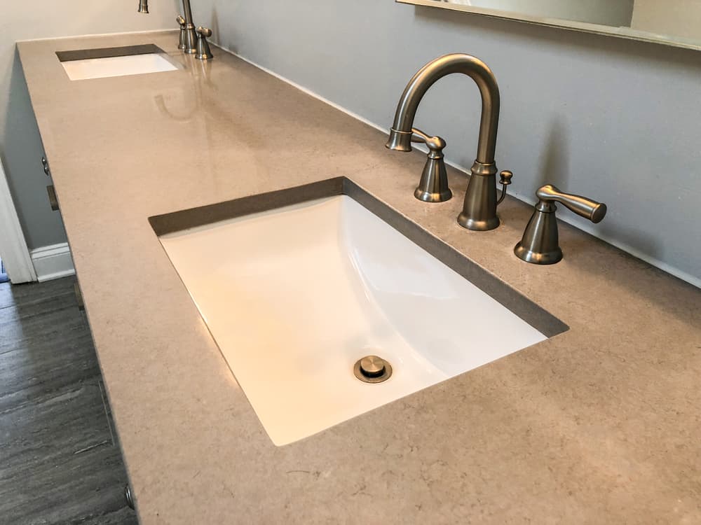 Modern bathroom with dual sinks, sleek beige countertop, and brushed nickel fixtures against a neutral wall, creating a clean, elegant atmosphere.