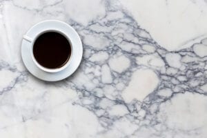 White cup filled with black coffee on a smooth, white marble table with intricate gray veining, creating a calm and sophisticated tone.