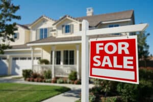 A residential property featuring a 'For Sale' sign, set against a backdrop of a clear blue sky and well-maintained landscaping.