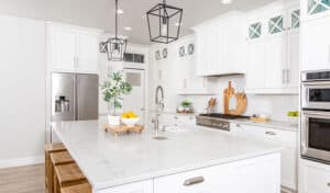 Bright, modern kitchen with white cabinets, stainless steel appliances, and a marble island. Decor includes plants and citrus fruits; a clean, fresh atmosphere.