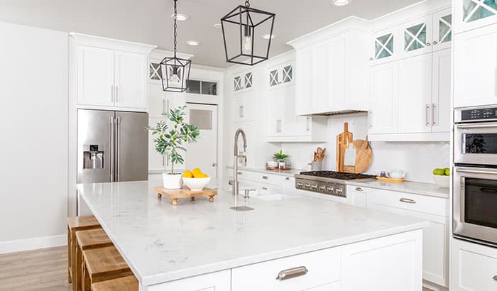 Bright, modern kitchen with white cabinets, stainless steel appliances, and a marble island. Decor includes plants and citrus fruits; a clean, fresh atmosphere.