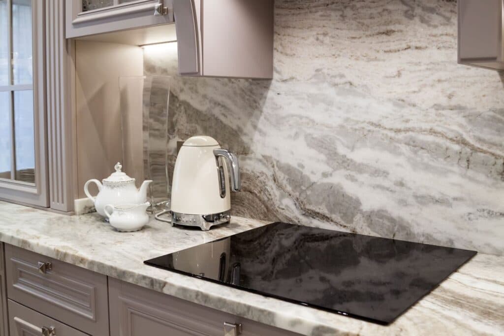 Modern kitchen counter with marble backsplash, electric kettle, teapot, and stovetop.