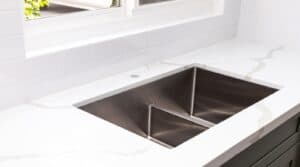 Modern kitchen sink with white countertop and tiled backsplash.