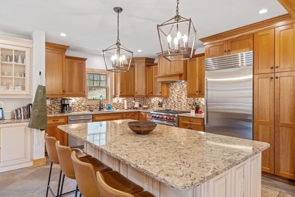 Modern kitchen with warm wood cabinets, granite island, leather bar stools, mosaic tile backsplash, and stainless steel appliances