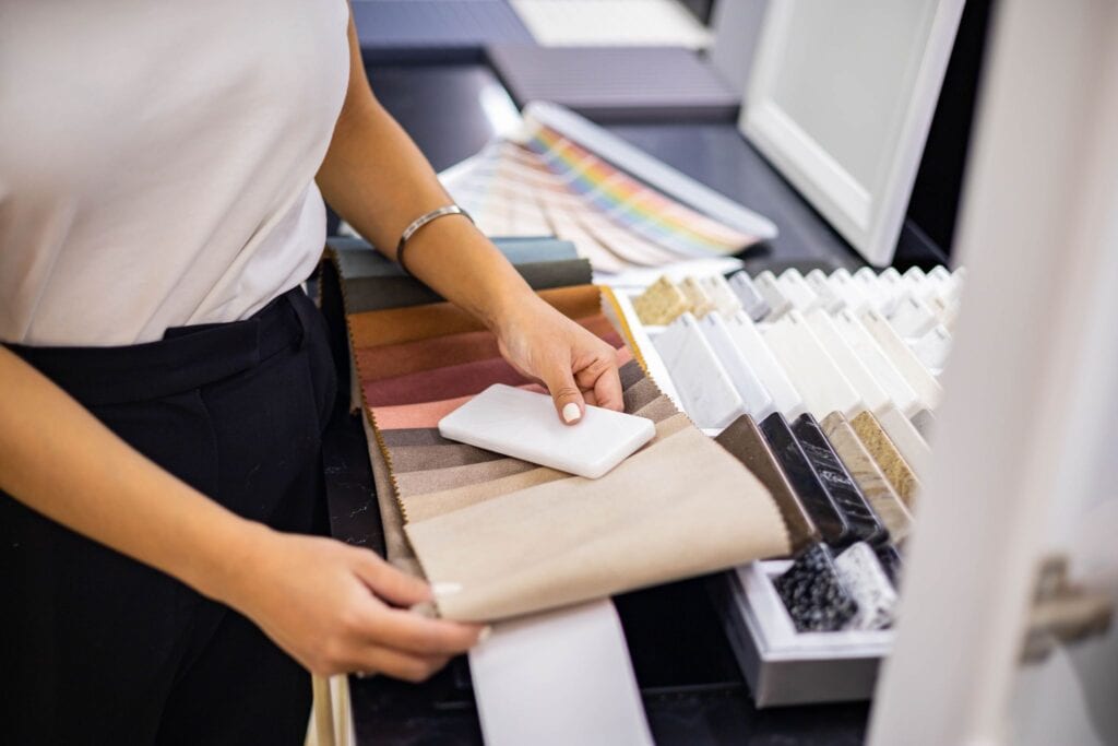 An interior designer comparing fabric swatches with stone and countertop samples in a design showroom.