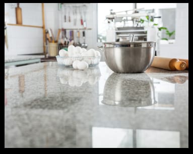 A kitchen counter with a bowl of eggs and a mixing bowl on natural marble countertops.
